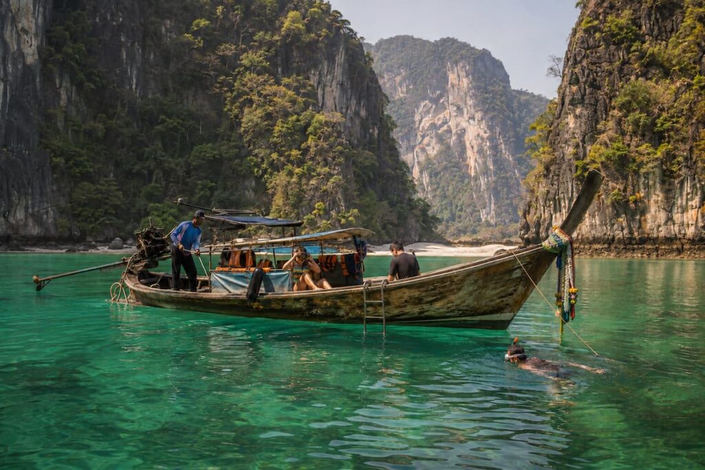 Traveller snorkelling beside a traditional longtail boat in a limestone bay in Southern Thailand