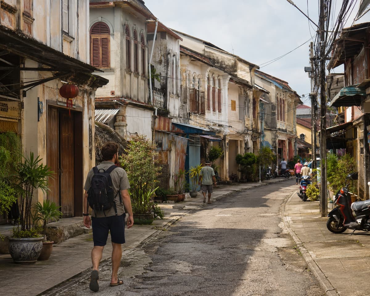 Traveller walking along a historic street lined with shophouses and scooters in Southeast Asia