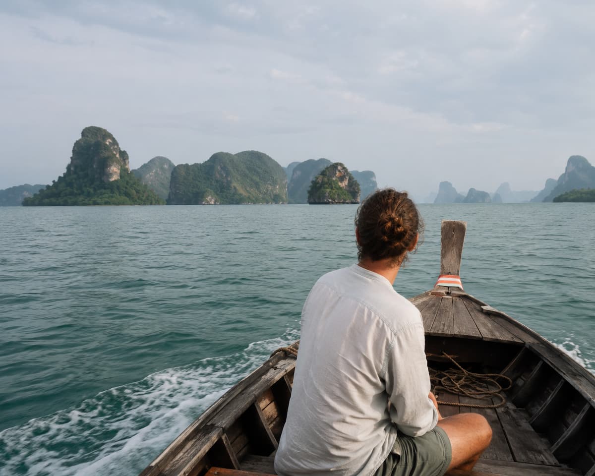 Traveller seated in a traditional longtail boat approaching limestone islands in Southern Thailand for home page hero illustrating Discover Southeast Asia