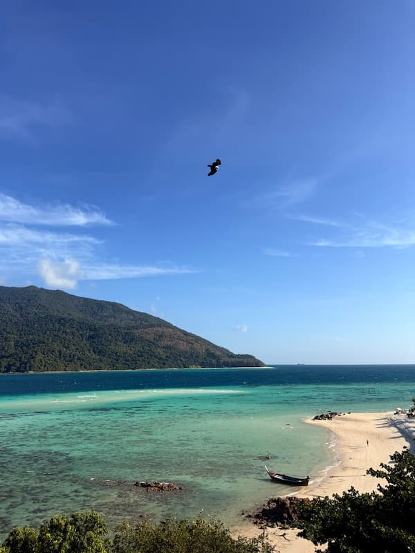 Southern Thailand travel guide view of clear turquoise water, a sandy beach and longtail boat at Koh Lipe.