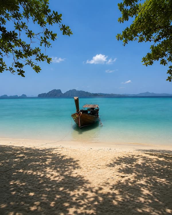 Southern Thailand travel guide view of a longtail boat beside a quiet beach in the Trang islands.