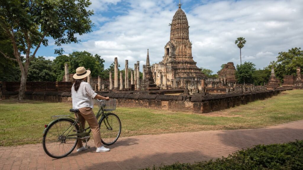 Traveller pauses with a bicycle to view Wat Mahathat in Sukhothai Historical Park, Thailand.