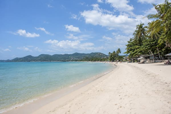 Thailand travel guide view along Chaweng Beach with calm blue water, white sand and tropical beachfront on Koh Samui.