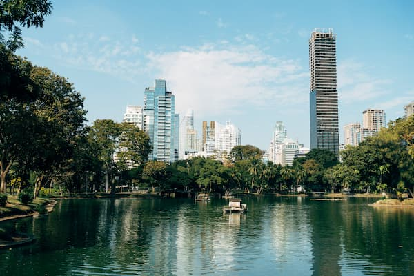 Thailand travel guide view across Lumphini Park lake towards Bangkok’s modern city skyline.