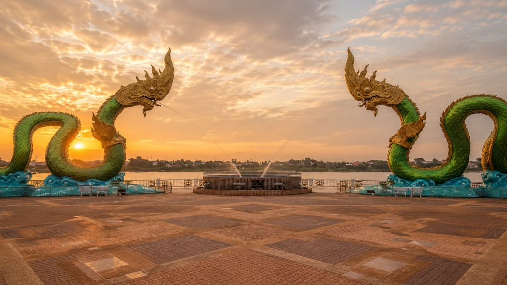 Thailand travel guide view of sunset behind the twin Naga statues beside the Mekong River in Nong Khai.