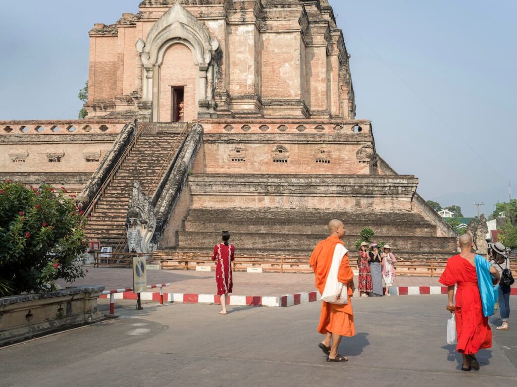 Buddhist monks walking beside the historic Wat Chedi Luang temple in Chiang Mai, Thailand.