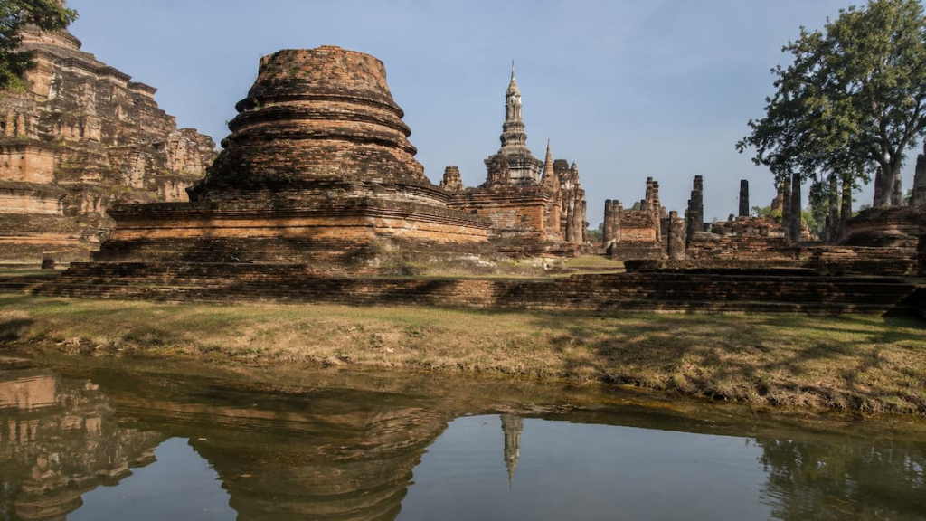 Thailand travel guide view of ancient temple ruins reflected in water at Wat Mahathat in Sukhothai Historical Park.