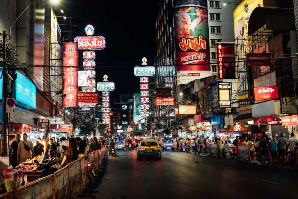 Busy street-food stalls and illuminated signs along Yaowarat Road in Bangkok at night.