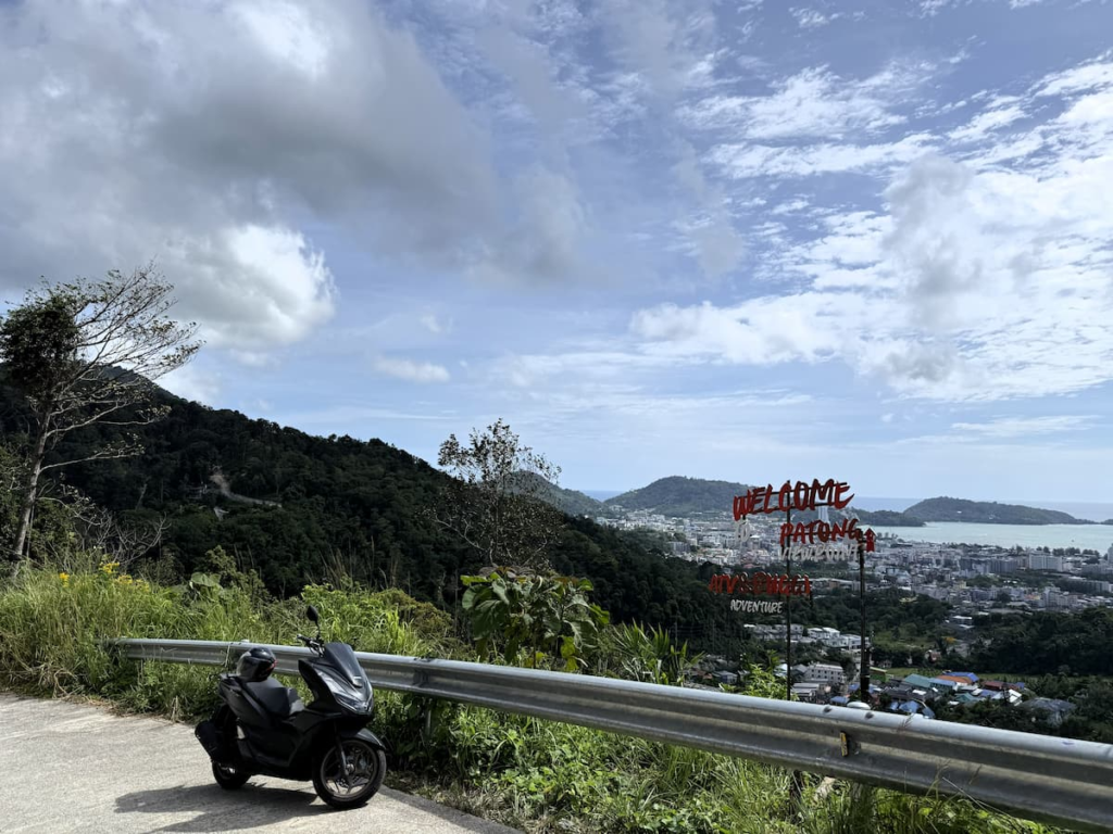 Roadside stopping area at Patong Viewpoint with a scooter, guardrail and view over Patong