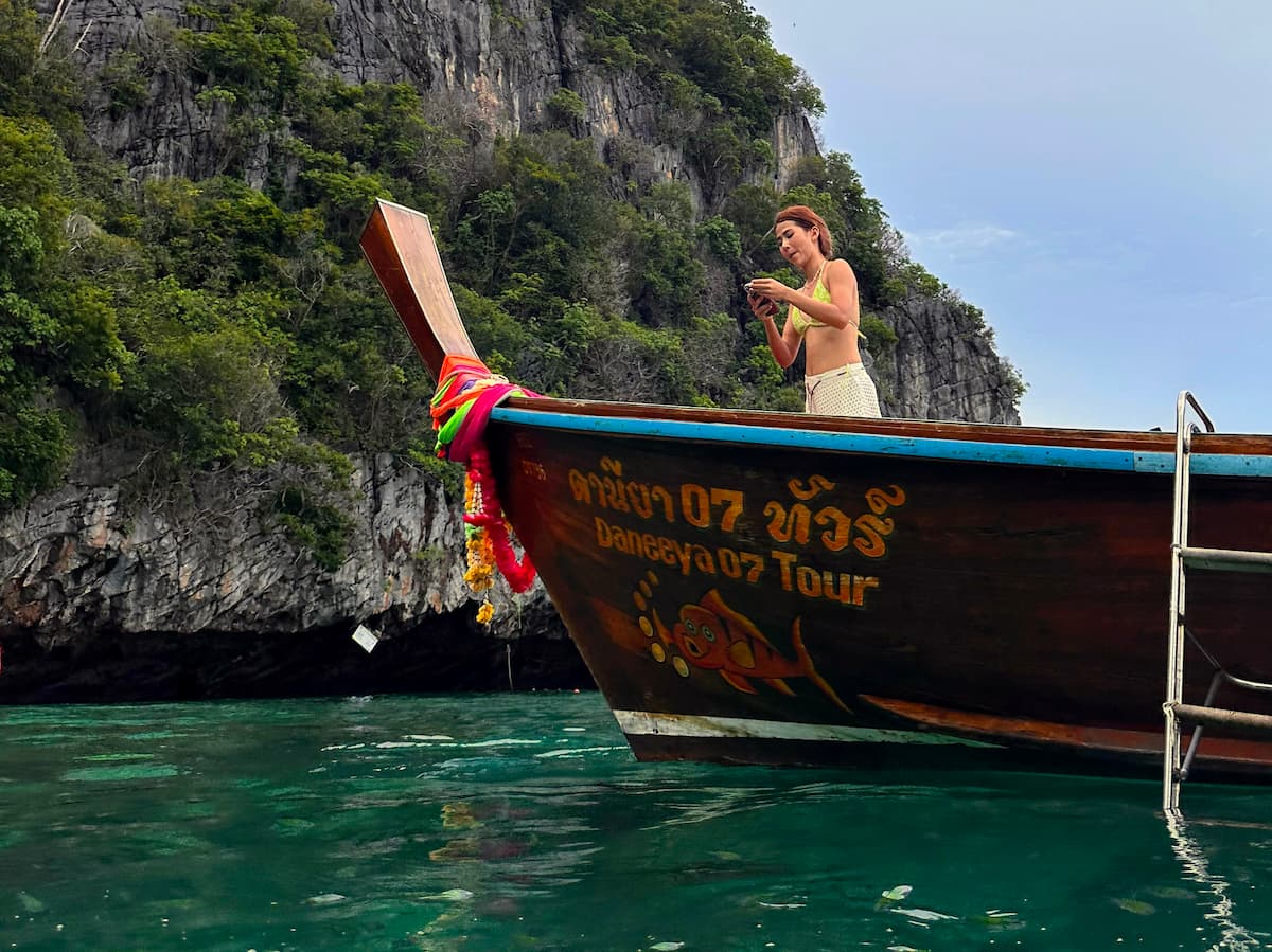Traveller aboard a traditional longtail boat beside limestone cliffs in Southern Thailand