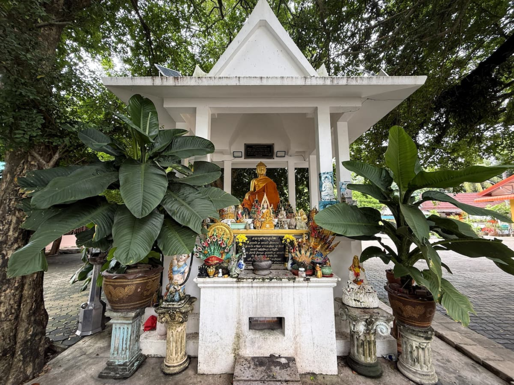 Small devotional shrine among plants at Wat Thipphaksong Laem Phet in Patong